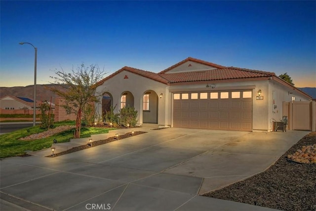 mediterranean / spanish-style home featuring an attached garage, stucco siding, concrete driveway, and a tiled roof