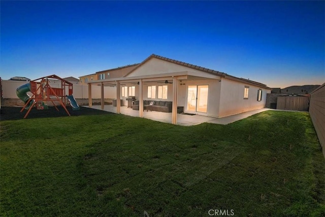 back house at dusk with a lawn, a patio, and a playground