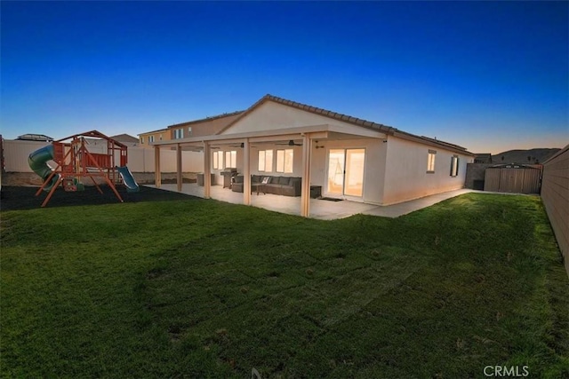 back of house at dusk with a playground, a fenced backyard, a yard, stucco siding, and a patio area