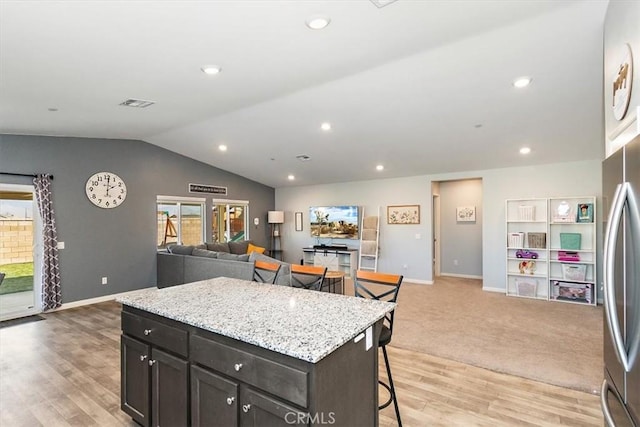 kitchen featuring a center island, freestanding refrigerator, open floor plan, vaulted ceiling, and a kitchen breakfast bar