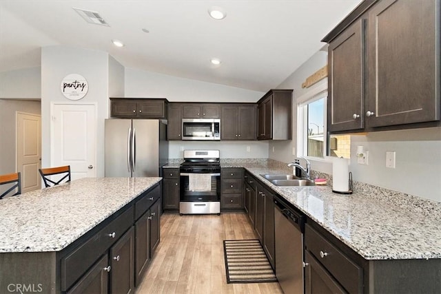 kitchen with lofted ceiling, stainless steel appliances, a kitchen island, a sink, and light wood finished floors