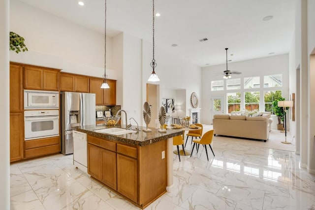 kitchen with white appliances, a high ceiling, an island with sink, decorative backsplash, and decorative light fixtures