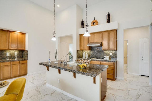 kitchen featuring a kitchen island with sink, hanging light fixtures, a towering ceiling, and a kitchen bar