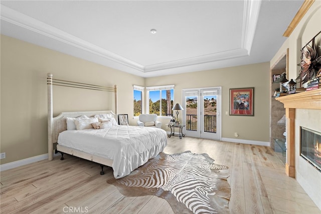 bedroom featuring light hardwood / wood-style floors, a tile fireplace, a raised ceiling, and access to exterior