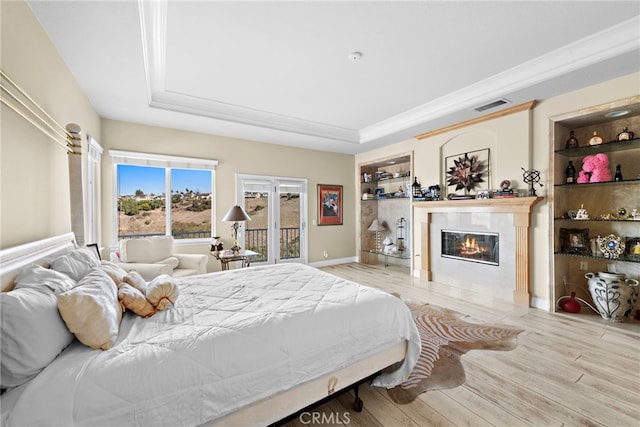 bedroom with a tile fireplace, ornamental molding, access to outside, a raised ceiling, and light wood-type flooring