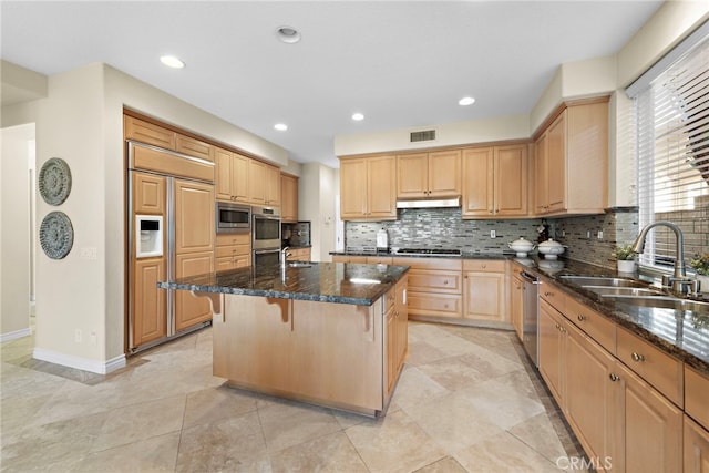 kitchen with sink, a breakfast bar, dark stone countertops, a center island, and built in appliances