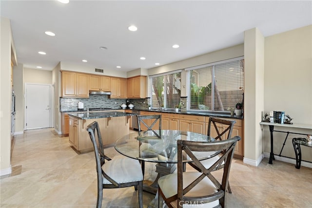 kitchen with a breakfast bar, tasteful backsplash, a center island, dark stone countertops, and stainless steel dishwasher