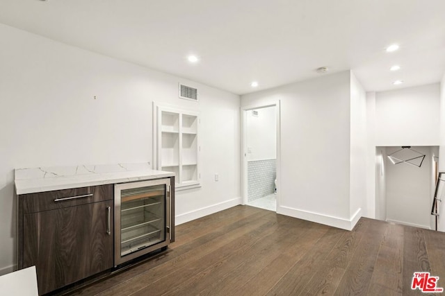 bar featuring light stone countertops, dark brown cabinets, dark wood-type flooring, and wine cooler