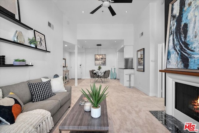 carpeted living room featuring ceiling fan and a towering ceiling