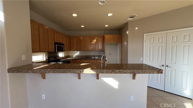 kitchen featuring a breakfast bar, sink, light tile patterned floors, kitchen peninsula, and stainless steel appliances