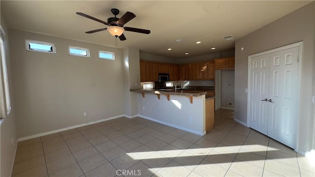 kitchen featuring sink, a kitchen bar, light tile patterned floors, ceiling fan, and kitchen peninsula