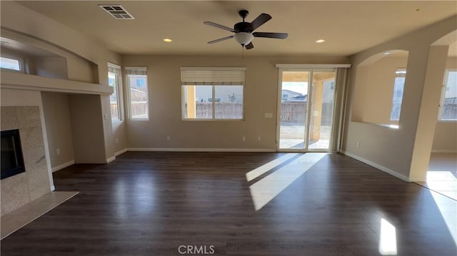 unfurnished living room featuring dark wood-type flooring, ceiling fan, plenty of natural light, and a tile fireplace