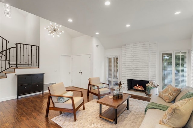 living room with wood-type flooring, high vaulted ceiling, a chandelier, and a fireplace