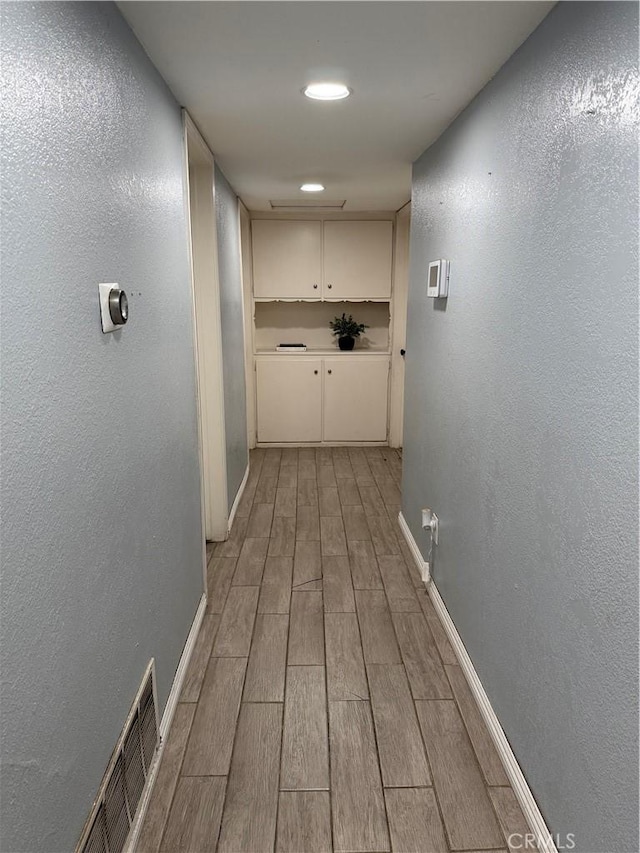 corridor featuring wood tiled floor, visible vents, baseboards, and a textured wall