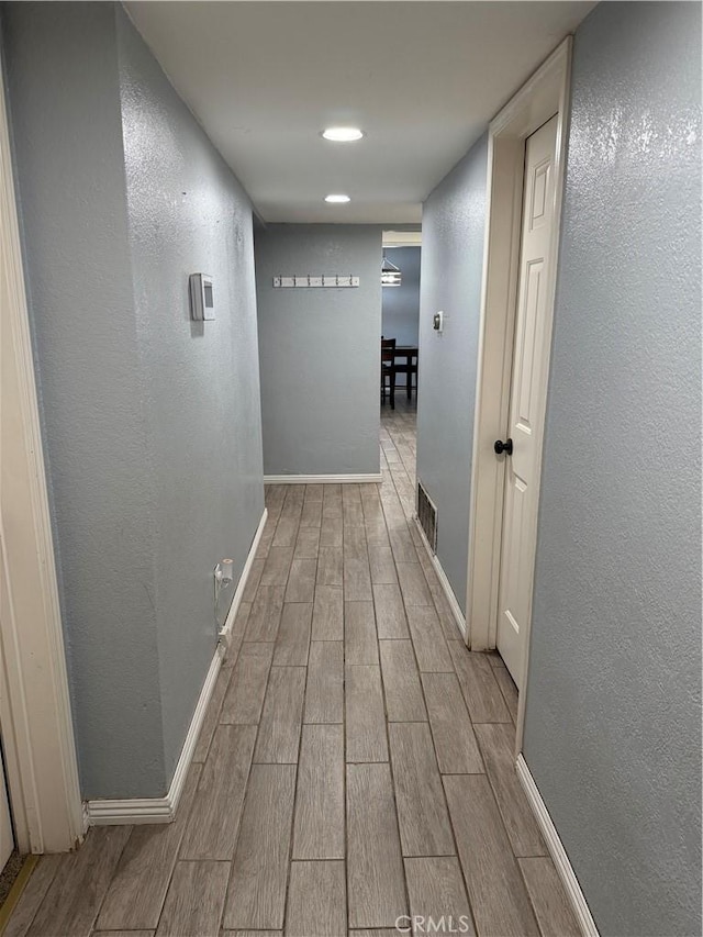 corridor featuring a textured wall, wood finish floors, visible vents, and baseboards