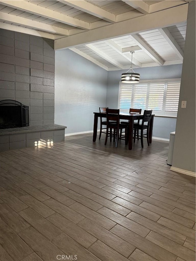 dining area with a fireplace, baseboards, wood finished floors, and beamed ceiling