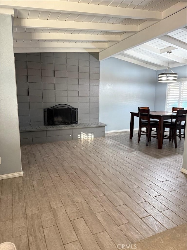 living room featuring a notable chandelier, wood finished floors, baseboards, beam ceiling, and a tiled fireplace