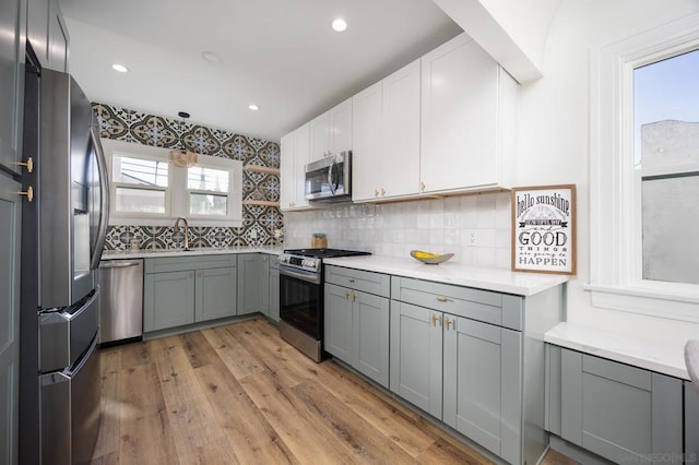 kitchen with light hardwood / wood-style flooring, appliances with stainless steel finishes, white cabinetry, gray cabinetry, and decorative backsplash