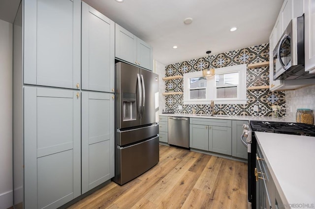 kitchen with appliances with stainless steel finishes, sink, gray cabinetry, hanging light fixtures, and light hardwood / wood-style flooring