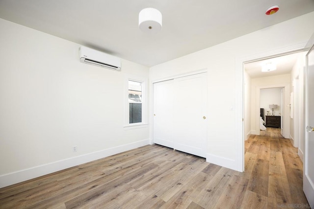 unfurnished bedroom with light hardwood / wood-style floors, a wall unit AC, and a closet