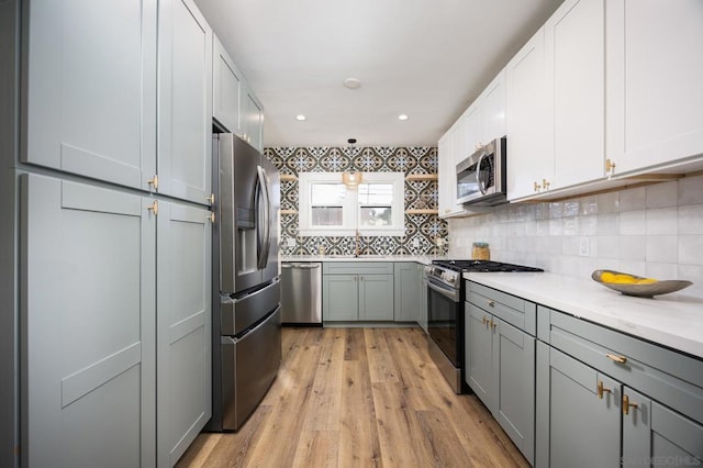 kitchen with gray cabinets, appliances with stainless steel finishes, light hardwood / wood-style floors, and decorative light fixtures