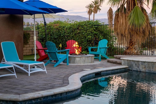 pool at dusk featuring a mountain view, a patio area, and an outdoor fire pit