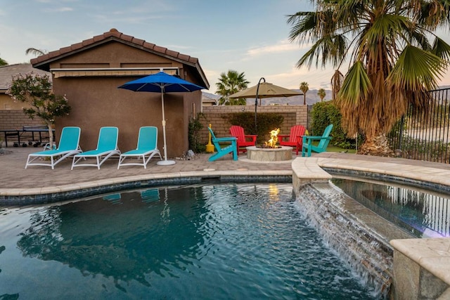 pool at dusk featuring an in ground hot tub, a patio, and an outdoor fire pit