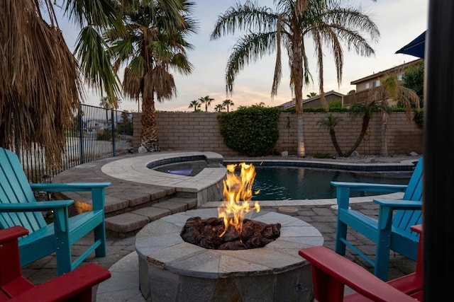 pool at dusk with a fire pit and a patio area