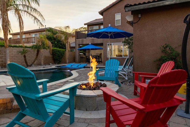 patio terrace at dusk featuring an outdoor fire pit and a fenced in pool