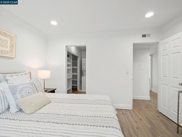 bedroom with hardwood / wood-style flooring, crown molding, a spacious closet, and a closet