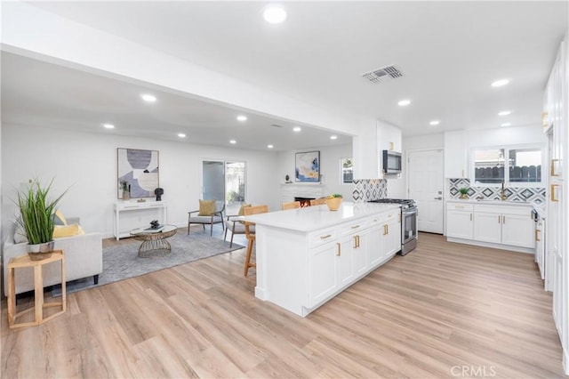 kitchen with a kitchen bar, white cabinetry, light hardwood / wood-style flooring, stainless steel appliances, and decorative backsplash