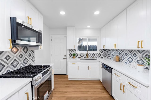 kitchen with sink, white cabinets, decorative backsplash, light hardwood / wood-style floors, and stainless steel appliances