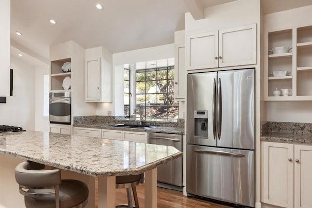 kitchen with appliances with stainless steel finishes, white cabinetry, sink, a kitchen breakfast bar, and light stone countertops