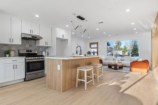 kitchen with a breakfast bar, white cabinetry, stainless steel range with gas cooktop, pendant lighting, and a kitchen island with sink