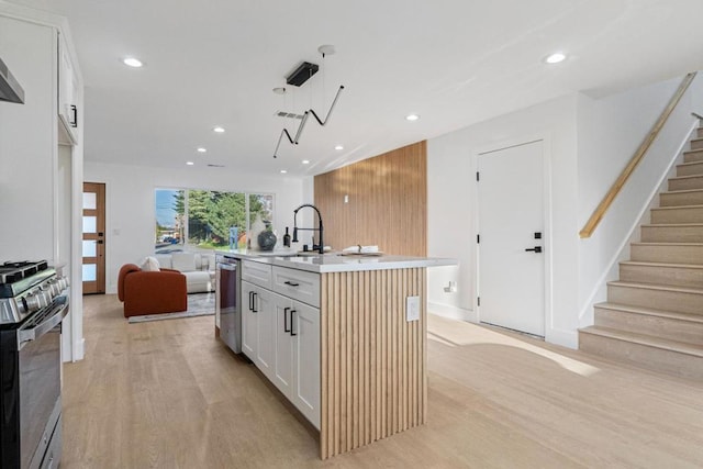 kitchen with white cabinetry, a center island with sink, appliances with stainless steel finishes, pendant lighting, and light hardwood / wood-style floors