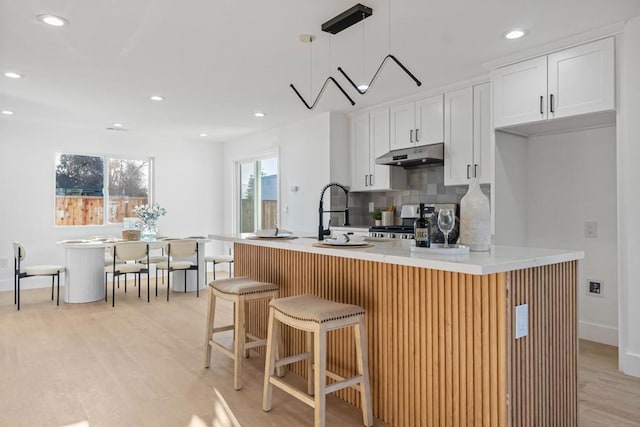 kitchen featuring pendant lighting, range, a kitchen breakfast bar, an island with sink, and white cabinets