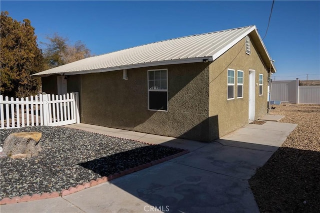 view of side of property with metal roof, fence, and stucco siding