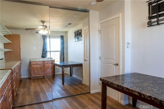 kitchen featuring brown cabinets, visible vents, dark wood-type flooring, a ceiling fan, and baseboards