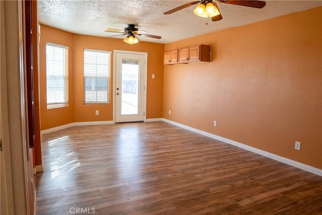 empty room featuring dark wood-style floors, a textured ceiling, a ceiling fan, and baseboards