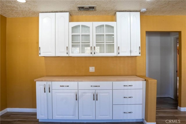 kitchen with dark wood-type flooring, white cabinets, visible vents, and glass insert cabinets