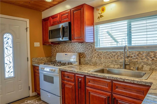 kitchen with reddish brown cabinets, tasteful backsplash, stainless steel microwave, white range with gas cooktop, and a sink