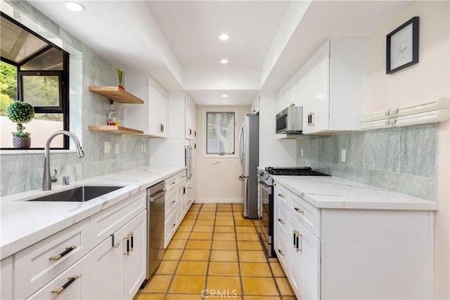 kitchen with appliances with stainless steel finishes, light stone counters, white cabinets, a raised ceiling, and sink