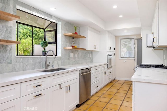 kitchen with stainless steel appliances, light stone countertops, white cabinets, decorative backsplash, and sink