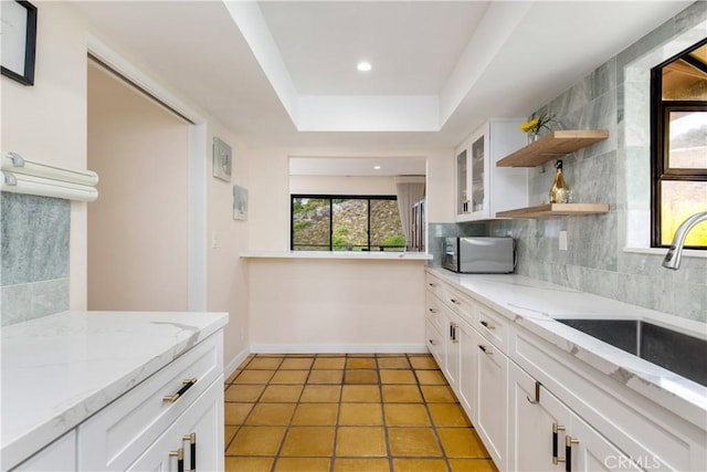 kitchen featuring white cabinetry, sink, backsplash, and light stone counters