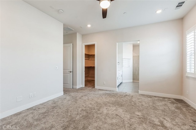 unfurnished bedroom featuring a walk in closet, light carpet, ceiling fan, and a closet