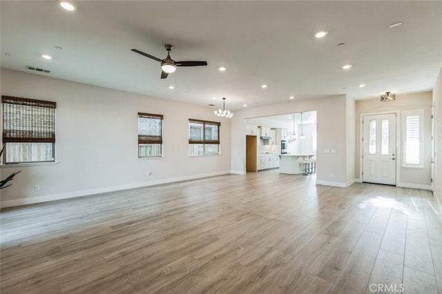 unfurnished living room featuring ceiling fan with notable chandelier and light hardwood / wood-style floors