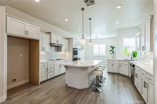 kitchen with light hardwood / wood-style flooring, appliances with stainless steel finishes, white cabinets, a kitchen island, and decorative light fixtures