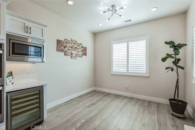 kitchen featuring wine cooler, white cabinetry, an inviting chandelier, stainless steel microwave, and light hardwood / wood-style floors