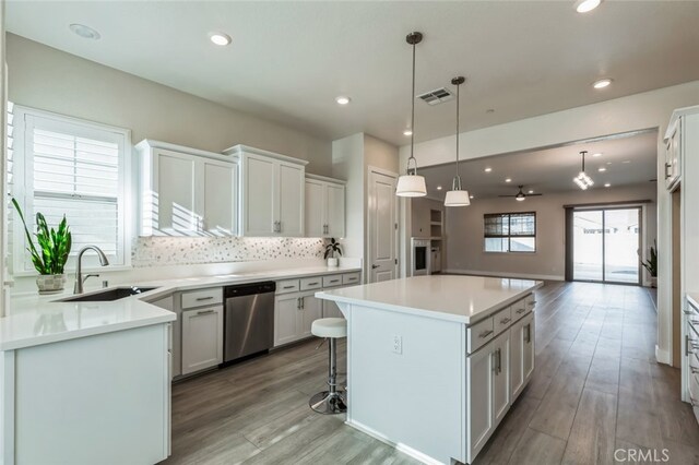 kitchen with sink, white cabinetry, hanging light fixtures, stainless steel dishwasher, and a kitchen island