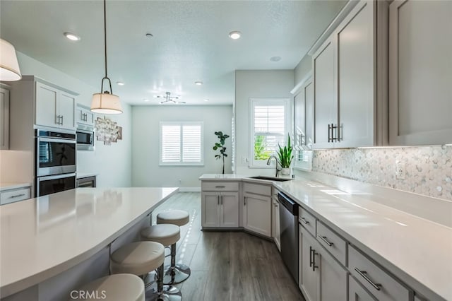 kitchen featuring sink, dark wood-type flooring, stainless steel appliances, decorative backsplash, and decorative light fixtures